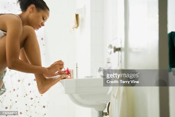 african woman painting toenails on bathroom sink - black painted toes stock-fotos und bilder