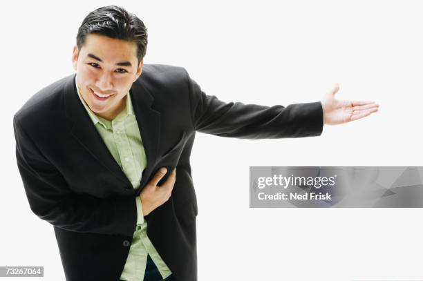 studio shot of young asian man smiling and bowing with arm out - bowing stock pictures, royalty-free photos & images