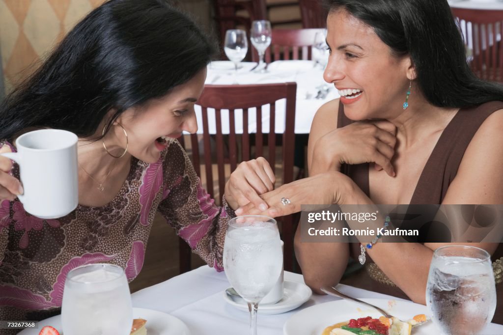 Hispanic woman showing ring to friend at restaurant