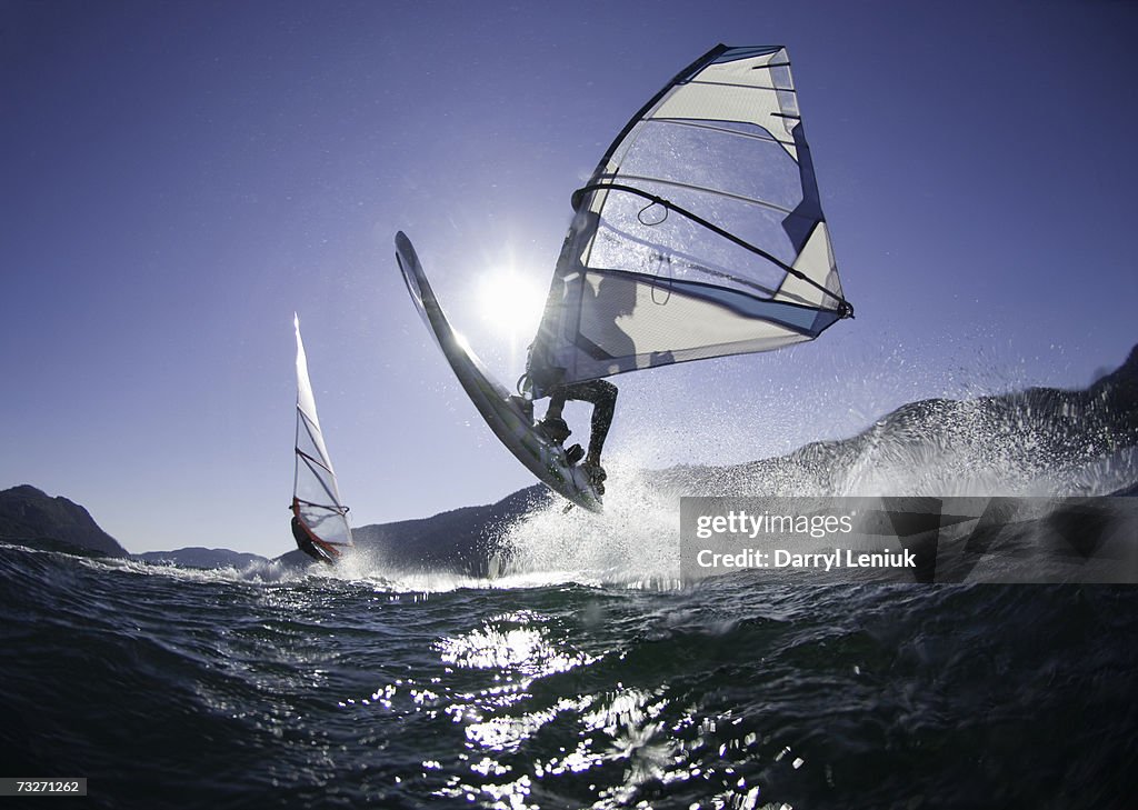 Man jumping wave on windsurf board, rear view