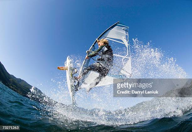 man jumping wave on windsurf board, low angle view - deporte acuático fotografías e imágenes de stock