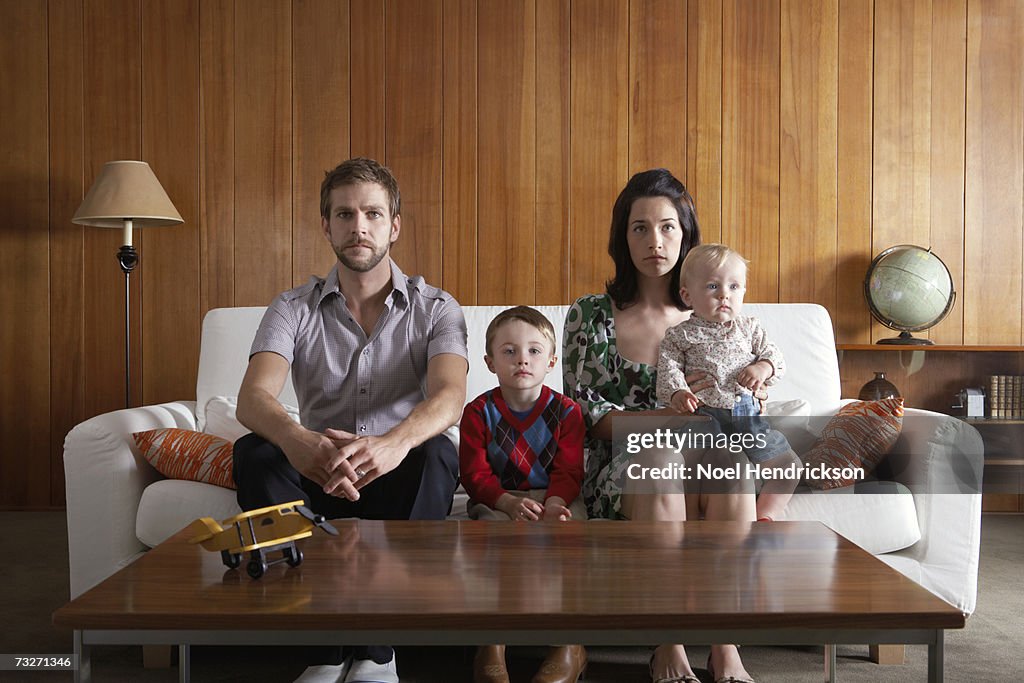 Parents with son (3-5), and baby girl (6-9 months) sitting on couch in living room