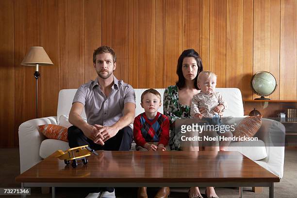 parents with son (3-5), and baby girl (6-9 months) sitting on couch in living room - bores stock pictures, royalty-free photos & images