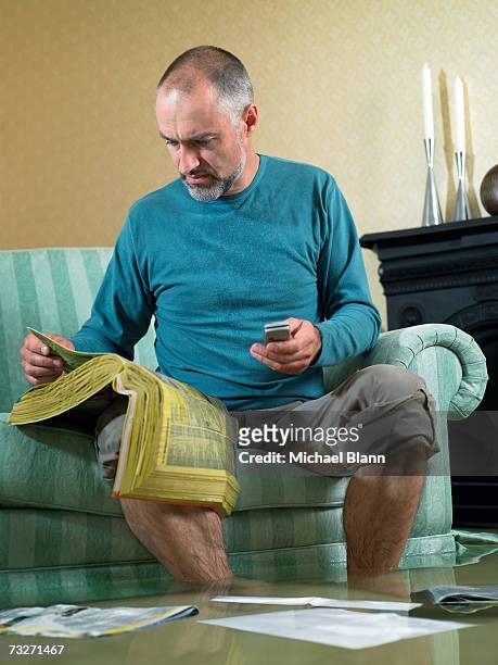 man sitting in flooded living room using phone - flooded room stock pictures, royalty-free photos & images