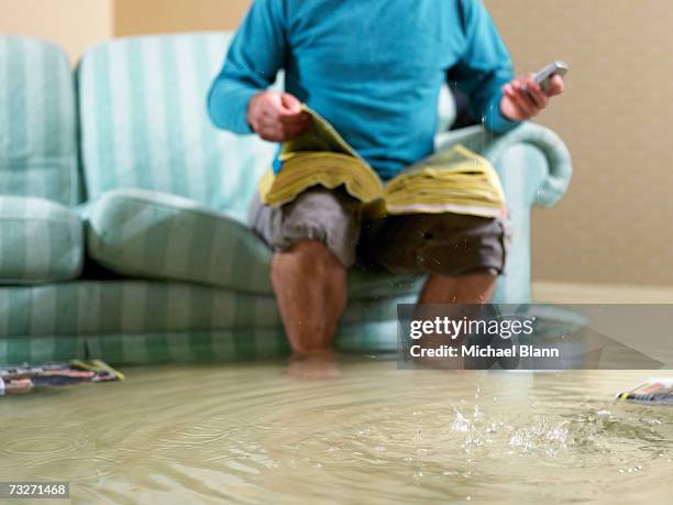 man sitting in flooded living room using phone, low section - flooded room stock-fotos und bilder