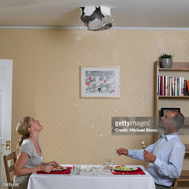 couple eating meal with foot coming through ceiling - inconvenience stock pictures, royalty-free photos & images
