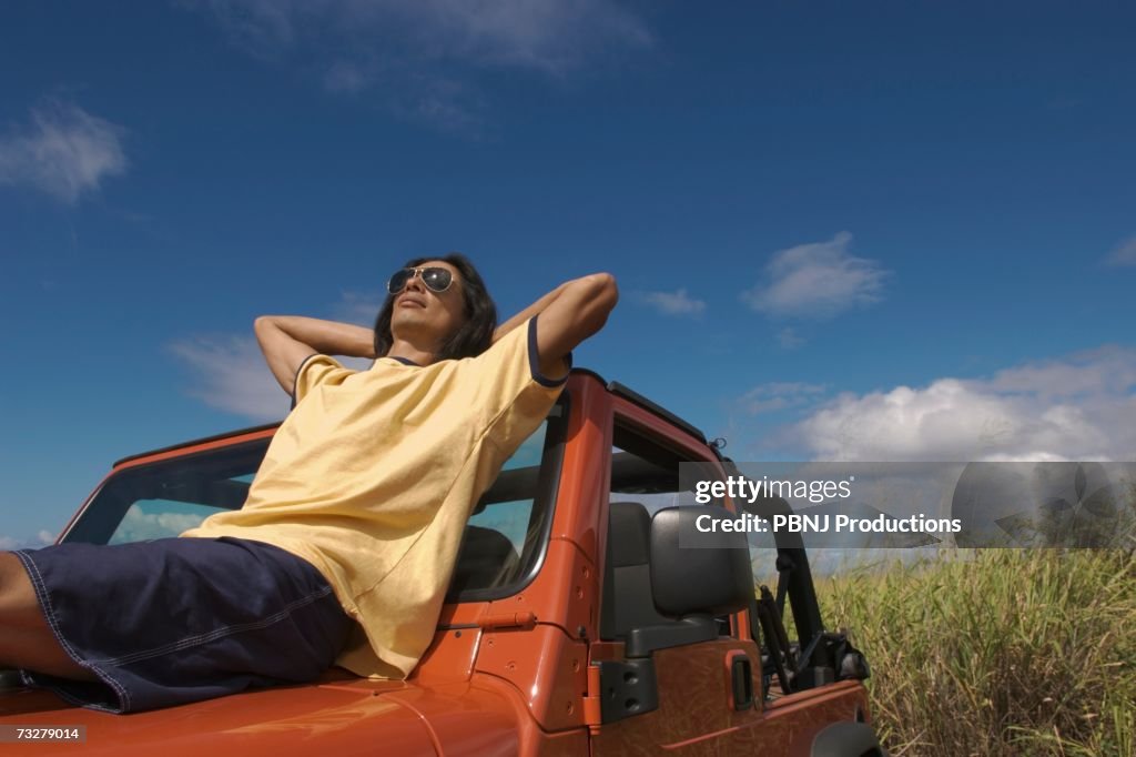 Man reclining on hood of jeep under blue sky