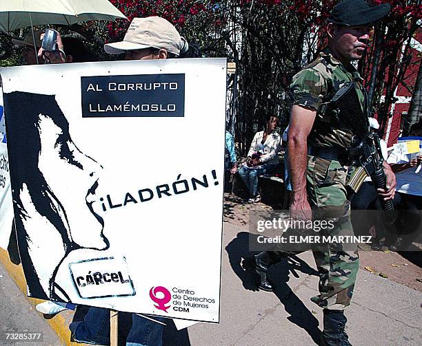 Tegucigalpa, HONDURAS: Un soldado camina frente a una mujer que sostiene una pancarta durante la "Marcha por la Integridad y contra la Corrupcion" en...