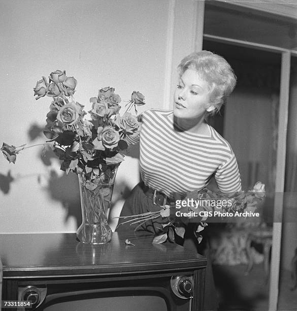 American film actress Kim Novak wears a striped jumper as she arrangers roses in a vase on top of her television set in her living room for an...