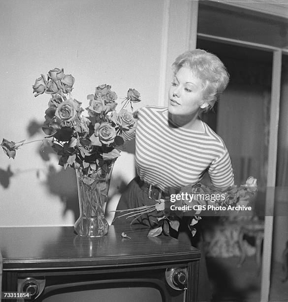 American film actress Kim Novak wears a striped jumper as she arrangers roses in a vase on top of her television set in her living room for an...