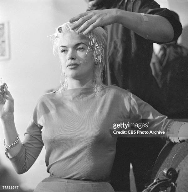 American film actress Jayne Mansfield sits and smokes a cigarette as a hair stylist readies her hair for her appearance on the CBS celebrity...