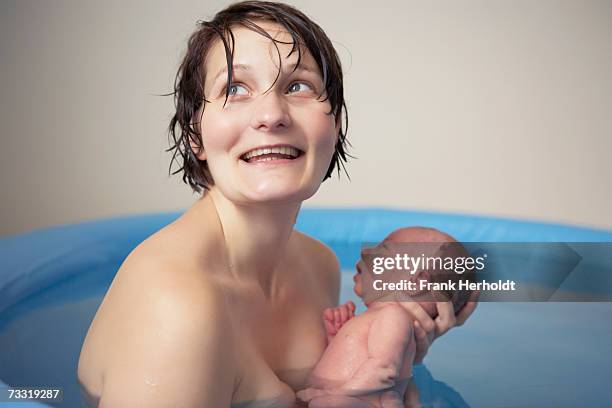 woman looking up holding newborn baby boy (0-3 months) in birthing pool - home birth stock-fotos und bilder