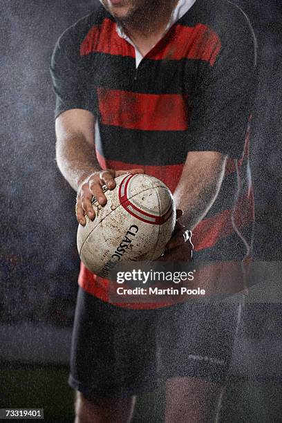 rugby player holding ball in rain, mid section - rugby ball stockfoto's en -beelden