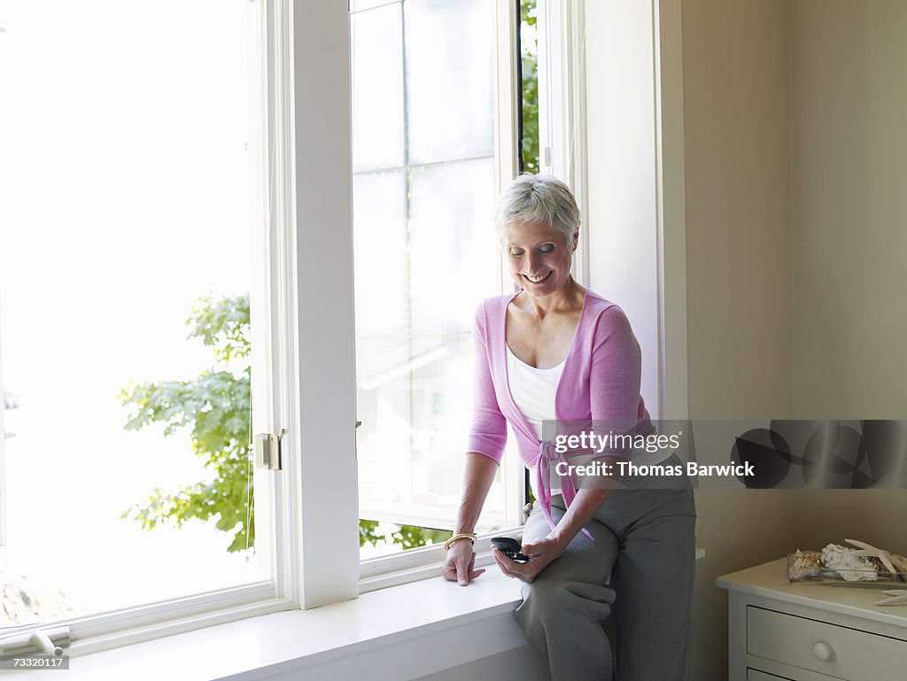 Senior woman at window using mobile phone