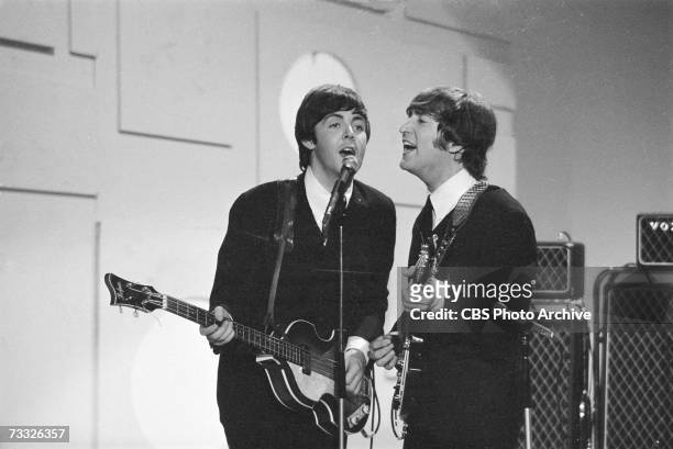 Members of the British rock band The Beatles, Paul McCartney and John Lennon , sing into a microphone as they play their instruments at the taping of...