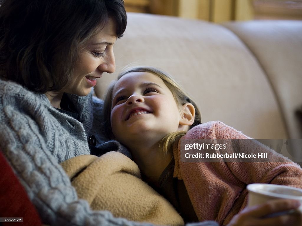 Woman with young girl snuggling on sofa