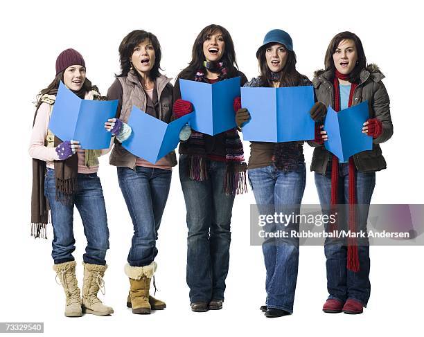 five women in winter coats singing with sheet music - christmas carols stock-fotos und bilder