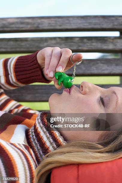 young woman lying on a wooden bench with a key ring pendant in her hand which she is kissing, close-up - woman frog hand stockfoto's en -beelden