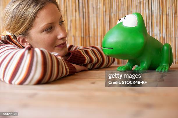 young woman smiling at an oversized toy frog, selective focus - woman frog hand stockfoto's en -beelden