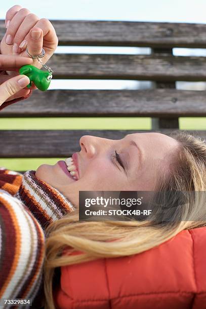 young woman lying on a wooden bench with a key ring pendant in her hand, close-up - woman frog hand stock-fotos und bilder