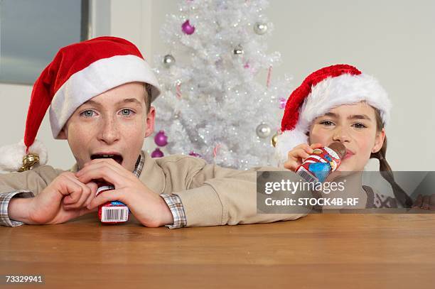 girl and boy wearing santa hats eating santa claus chocolates - santa leaning stock pictures, royalty-free photos & images