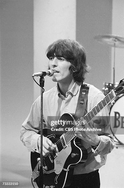 Member of the British rock band The Beatles George Harrison sings into a microphone as he plays his guitar at a rehearsal for the taping of a segment...