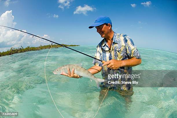 man with fishing rod, standing in emerald green water, holding bonefish - bone fish fotografías e imágenes de stock