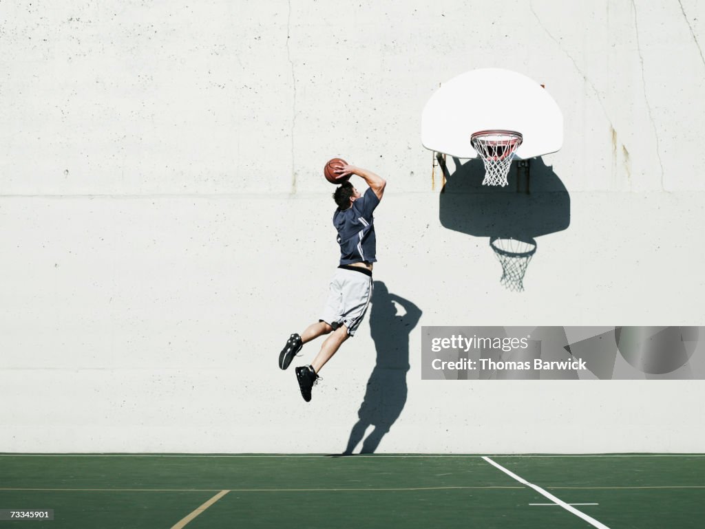 Man dunking basketball on outdoor court, mid-air, rear view