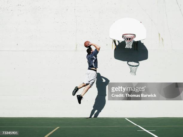 man dunking basketball on outdoor court, mid-air, rear view - dunk stockfoto's en -beelden