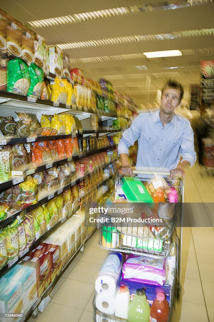 Man pushing laden shopping cart in supermarket aisle, blurred motion