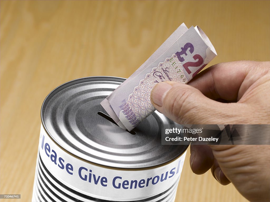 Person putting twenty pound note into donation tin