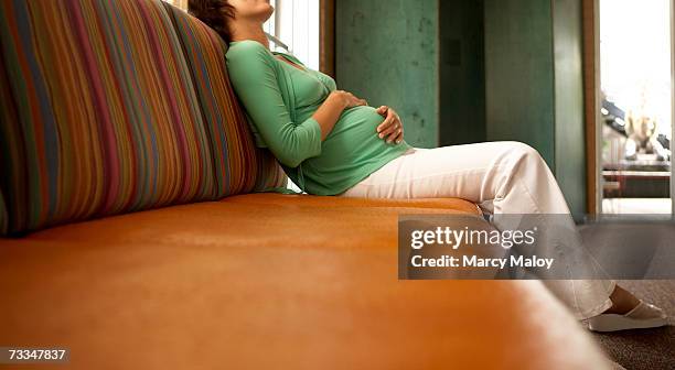 pregnant woman resting on couch in living room - holprig stock-fotos und bilder