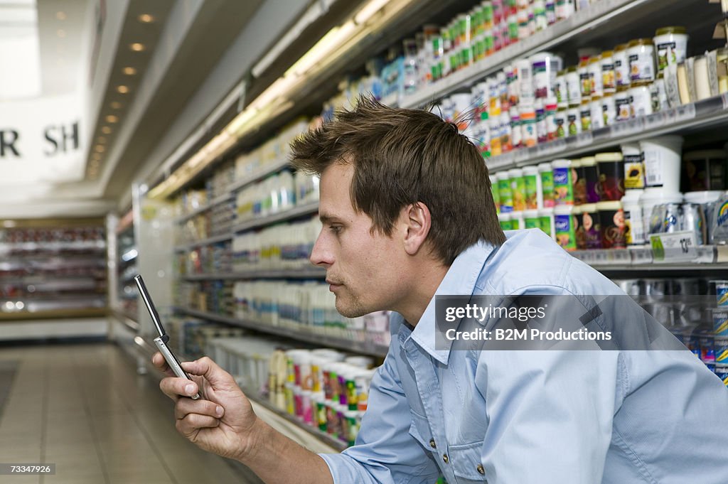 Man in supermarket using mobile phone, profile