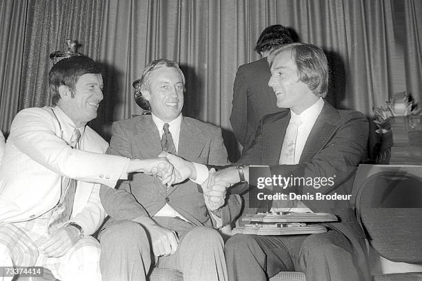 Ted Lindsay shakes hands with Guy Lafleur at an award ceremony. Jean Beliveau sits between them.