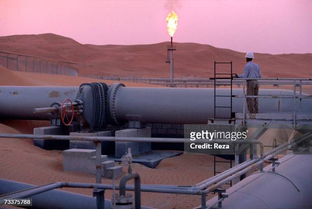 Worker stands at a pipeline, watching a flare stack at the Saudi Aramco oil field complex facilities at Shaybah in the Rub' al Khali desert on March...