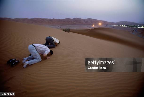 Men pray in the dunes just outside the Saudi Aramco oil field complex facilities at Shaybah in the Rub' al Khali desert on March 2003 in Shaybah,...