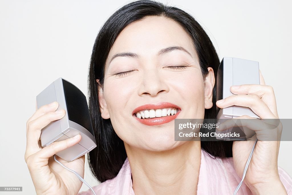 Close-up of a mid adult woman holding speakers upto her ear