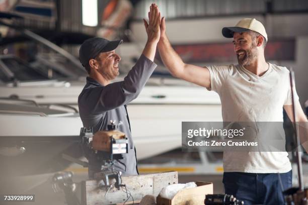 two men high fiving in boat repair workshop - repairing boat stock pictures, royalty-free photos & images