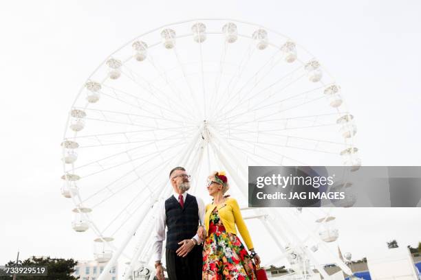 1950s vintage style couple strolling arm in arm by ferris wheel - 1950s couple stock pictures, royalty-free photos & images