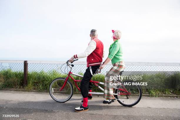 1950s vintage style couple looking out from tandem bicycle at coast - jag images photos et images de collection
