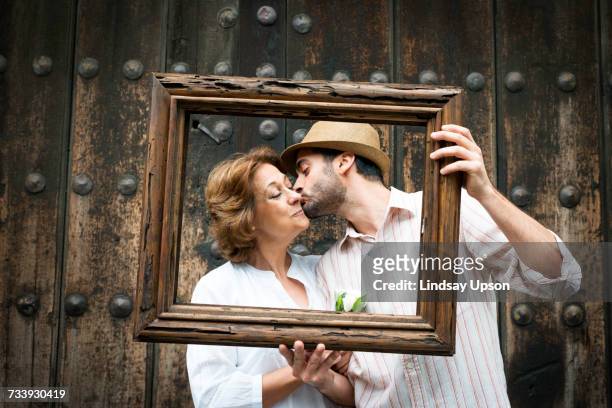portrait of adult son kissing mother on cheek, holding wooden frame in front of their faces, mexico city, mexico - family picture frame stockfoto's en -beelden