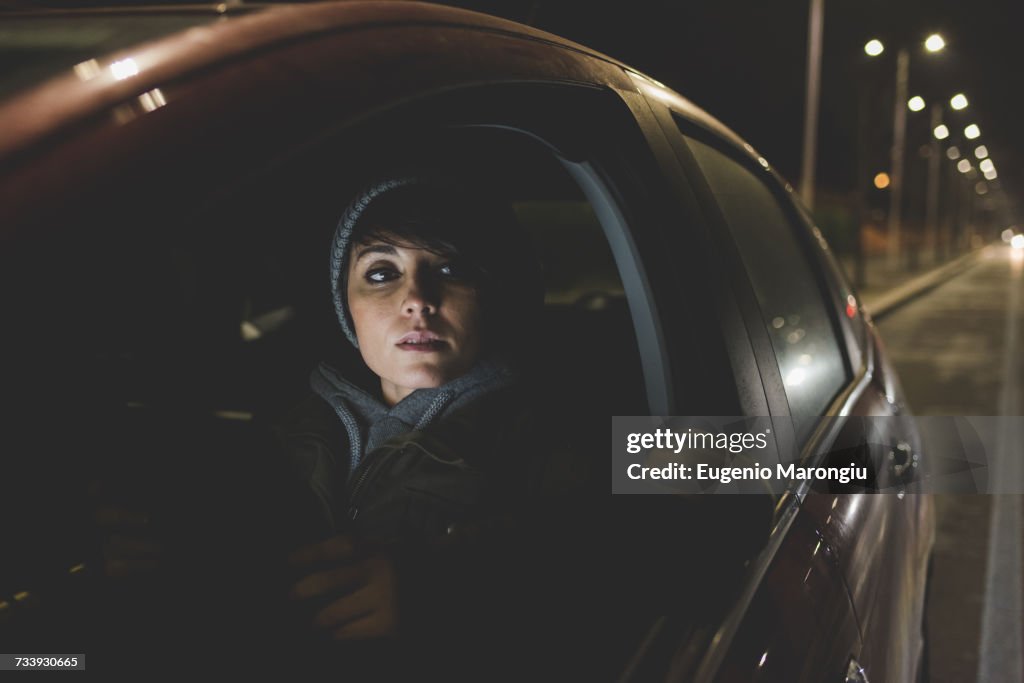 Woman looking out of car window on city roadside at night