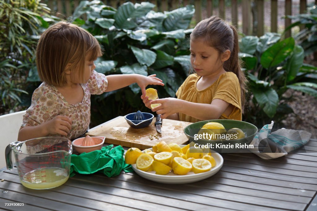 Two young sisters preparing lemon juice for lemonade at garden table