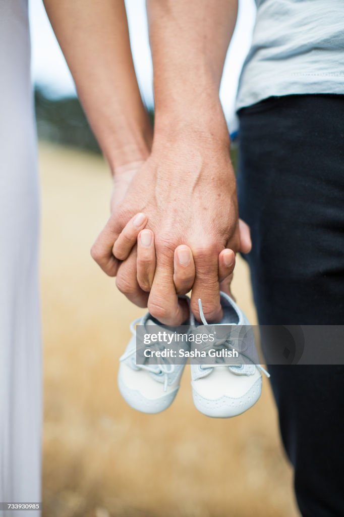 Couple holding hands, man holding baby shoes on fingers, close-up