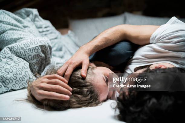 young couple lying in bed embracing face to face - man and woman cuddling in bed stock-fotos und bilder