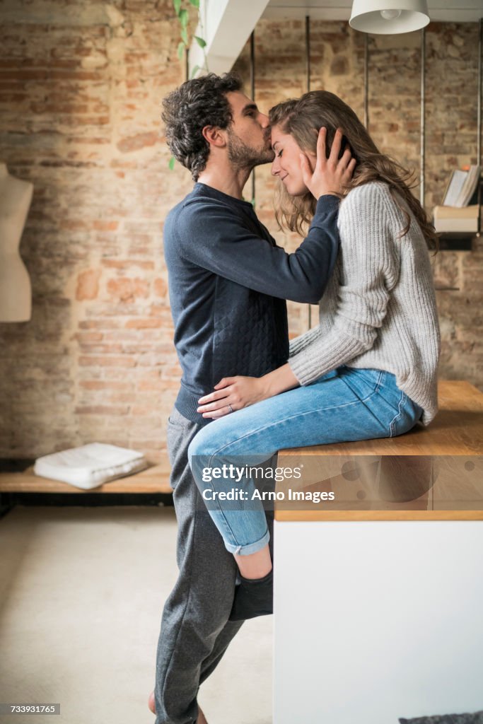 Young man kissing girlfriend on forehead at kitchen bench