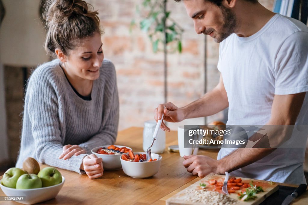 Young couple eating fruit breakfast at kitchen counter