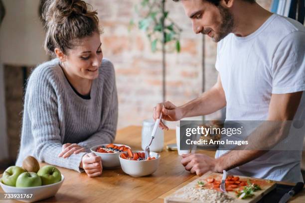 young couple eating fruit breakfast at kitchen counter - man eating woman out ストックフォトと画像