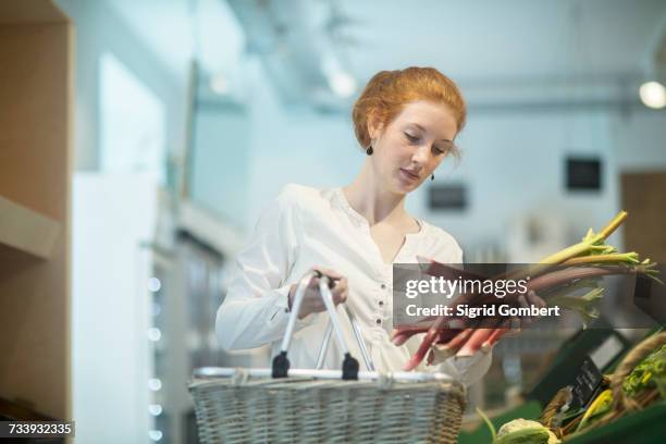 woman in shop holding shopping basket and rhubarb - rabarber stockfoto's en -beelden