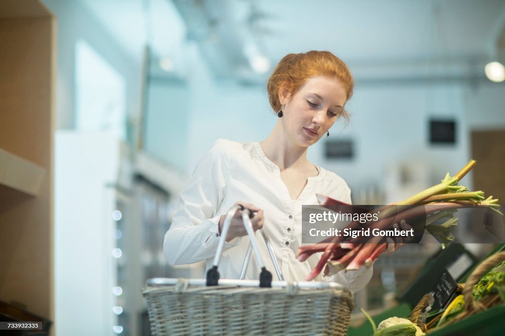 Woman in shop holding shopping basket and rhubarb